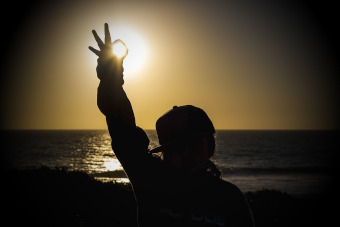 alt="jove davant una posta de sol recollint amb els dits la forma de l'astre"